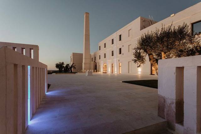 Industrial-chic estate lit at dusk with a tall chimney in Basilicata, Italy — unusual wedding venue